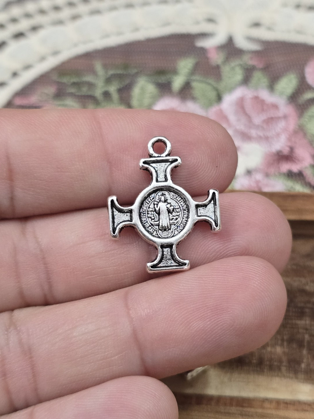 Benediktus-Medaille als Kreuz-Charm 22x18mm in Silber-Optik auf Hand gehalten als Größenvergleich.