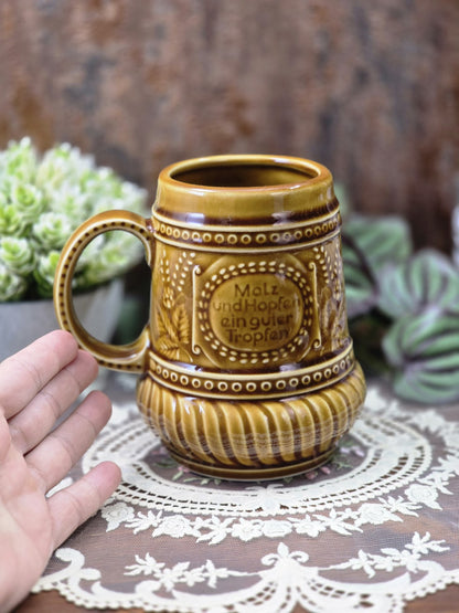 Vintage Steingut Bierkrug mit brauner Glasur, Schriftdekor und Hand als Größenvergleich neben dem Henkel