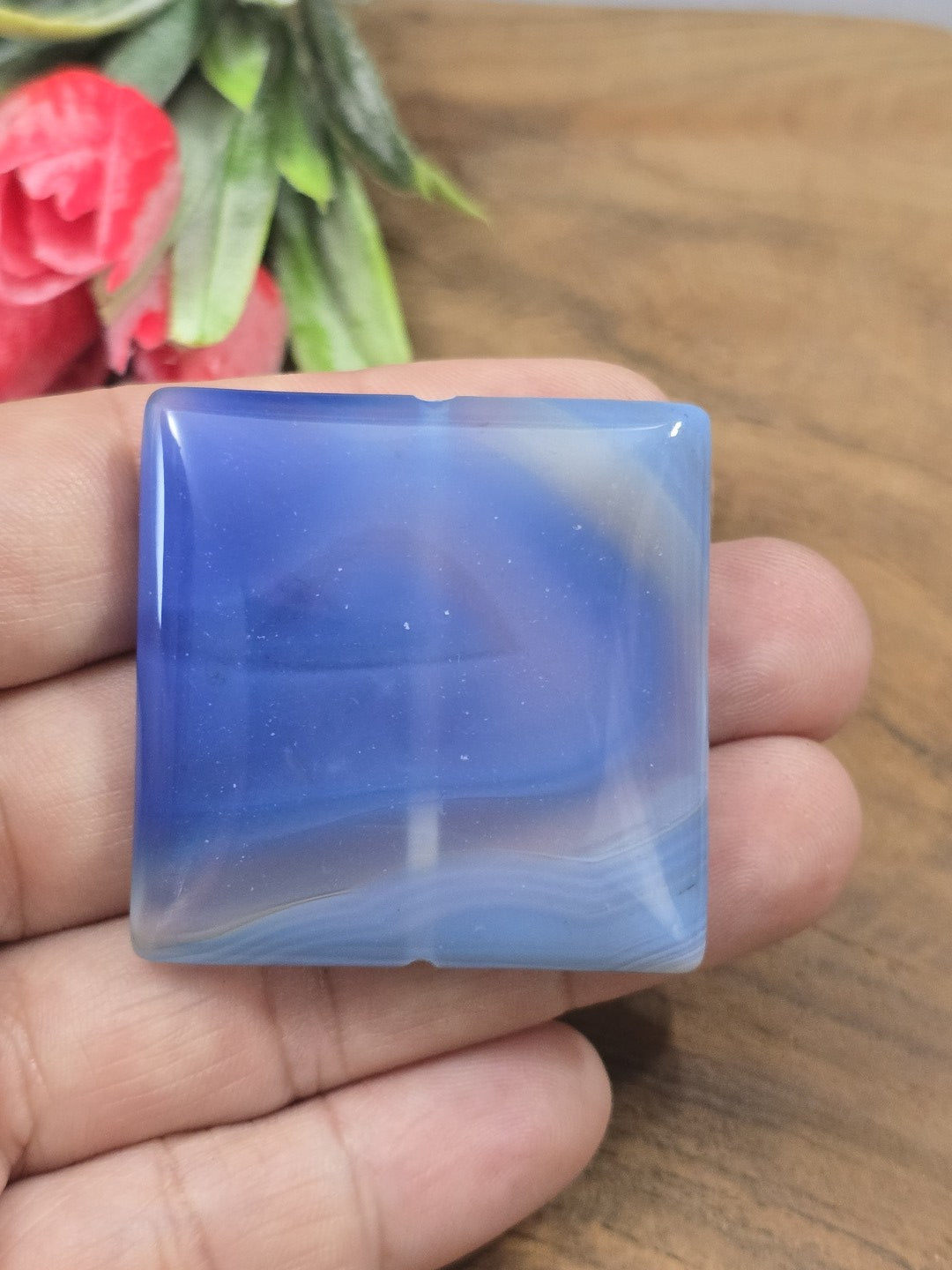 Polierter blauer Achat-Pendant in quadratischer Form auf der flachen Hand als Größenvergleich für Kettenanhänger.