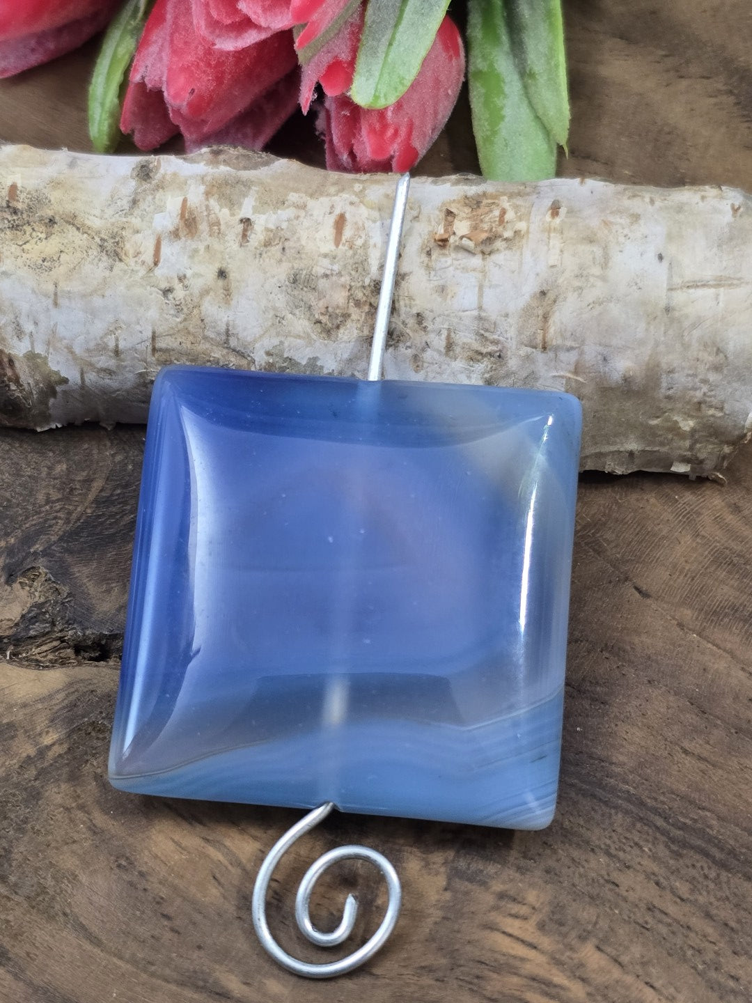 Aufgereihtes blaues Achat-Quadrat auf einem geschwungenen Metallstift zur Veranschaulichung der vertikalen Bohrung.