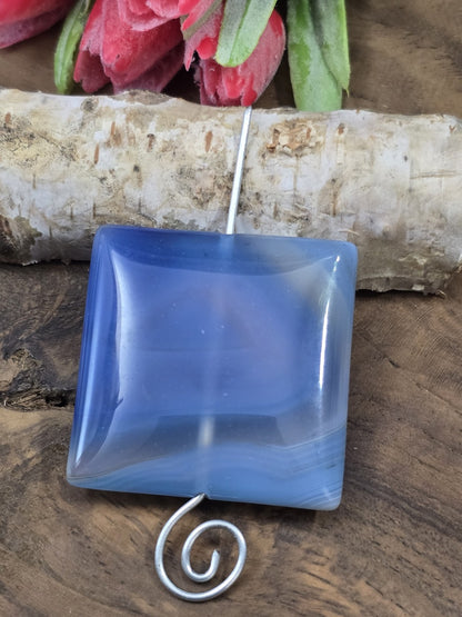 Aufgereihtes blaues Achat-Quadrat auf einem geschwungenen Metallstift zur Veranschaulichung der vertikalen Bohrung.
