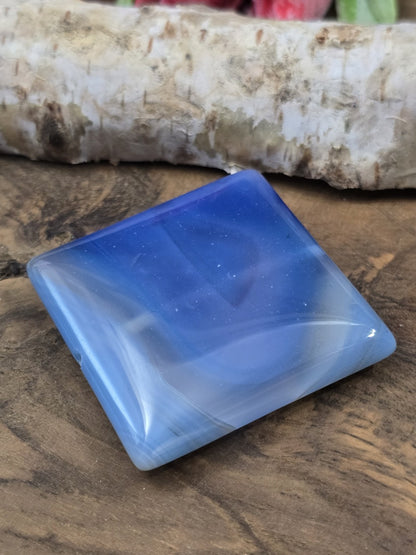 Schräge Liegeansicht des flachen quadratischen Achat-Edelsteins in Blau mit glänzender Oberfläche.