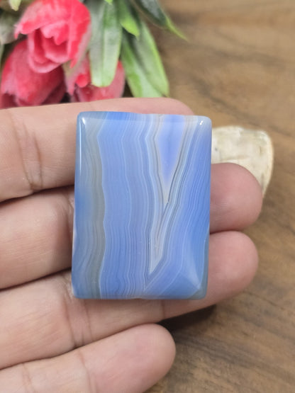 Polierter blauer Achat-Pendant in Rechteckform auf der flachen Hand als Größenvergleich für DIY-Schmuck.
