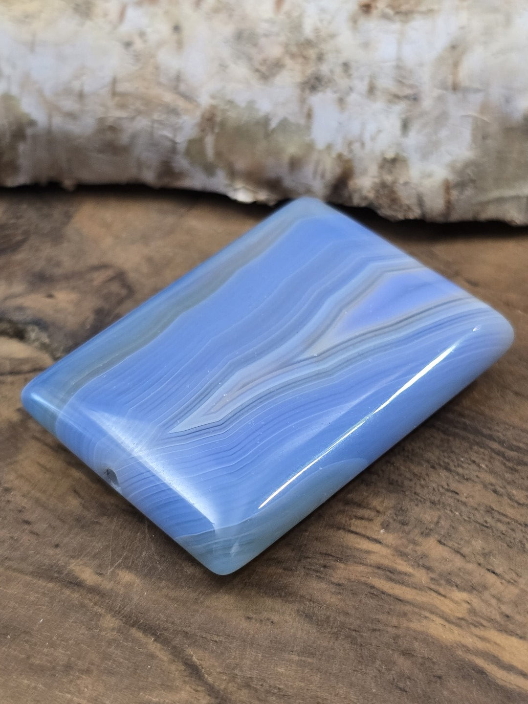 Schräge Liegeansicht der flachen rechteckigen Achatperle in Blau mit glänzender Oberfläche und Draufsicht auf das Bohrloch.