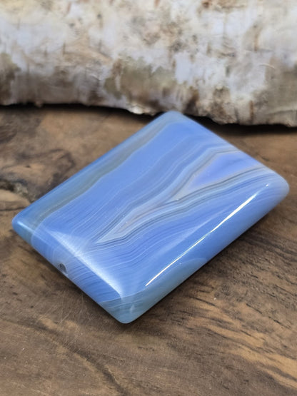 Schräge Liegeansicht der flachen rechteckigen Achatperle in Blau mit glänzender Oberfläche und Draufsicht auf das Bohrloch.