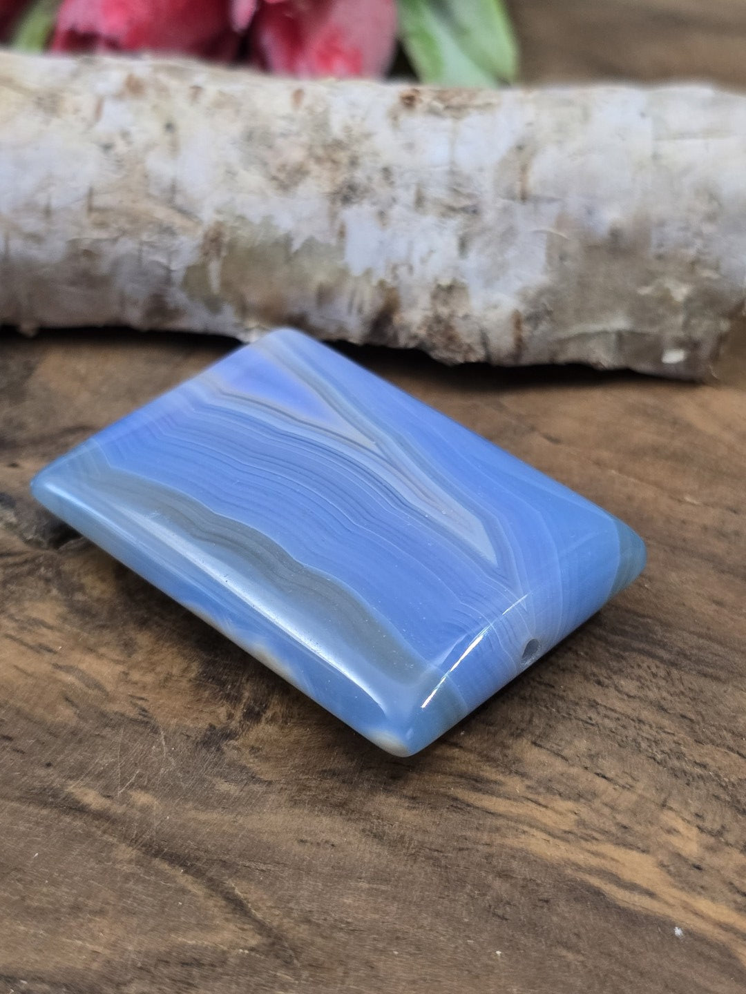 Perspektivische Seitenansicht des rechteckigen blauen Achat-Anhängers auf Holz mit Blick auf die untere Bohröffnung.