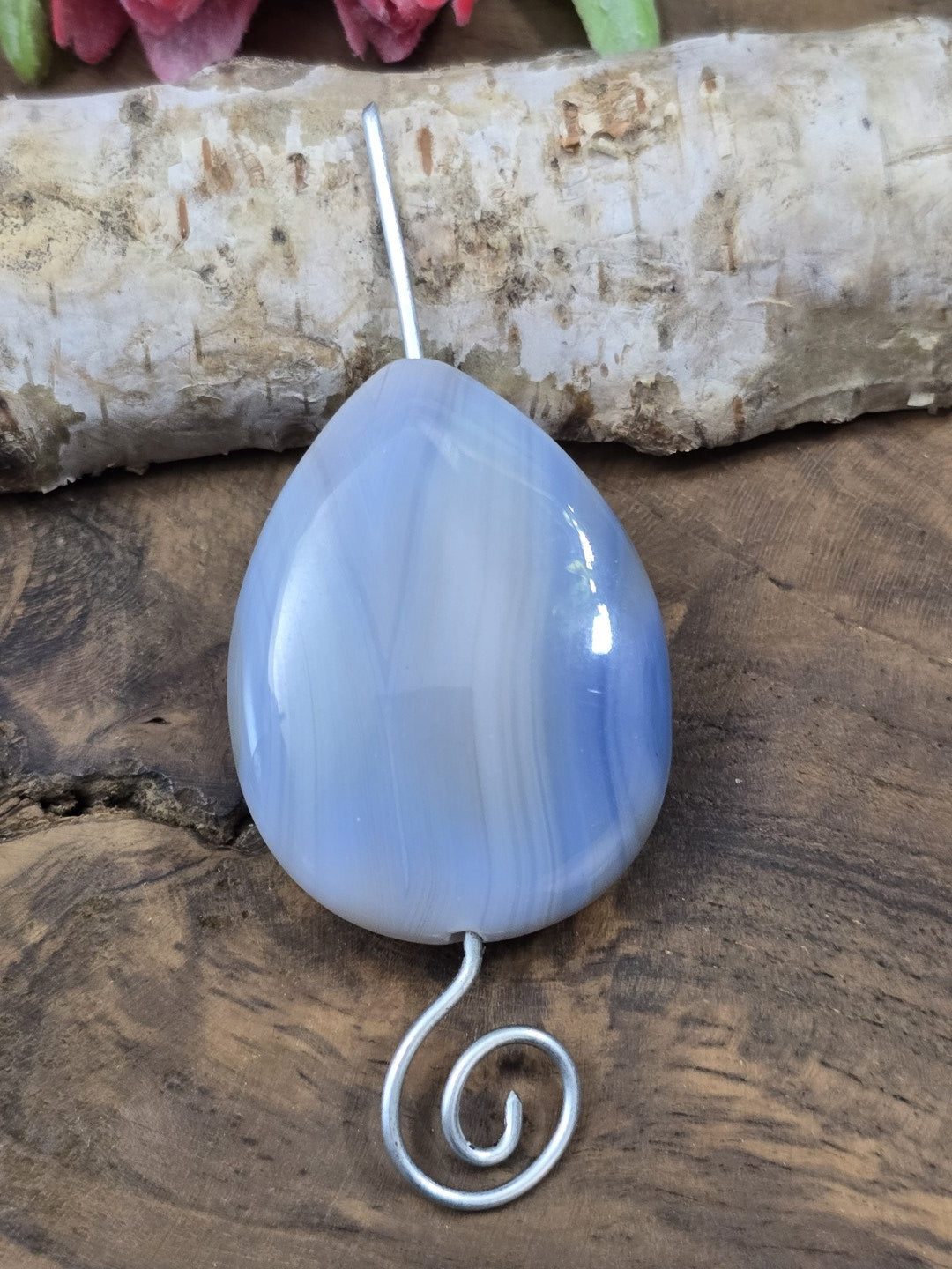 Gefädelter blauer Achat-Tropfen auf einem geschwungenen Metallstift zur Veranschaulichung der vertikalen Bohrung.