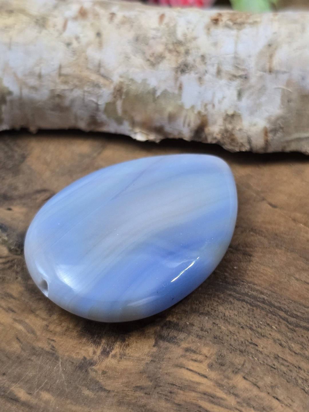 Schräge Liegeansicht des flachen blauen Achat-Edelsteins mit polierter Oberfläche und Lichtreflex.