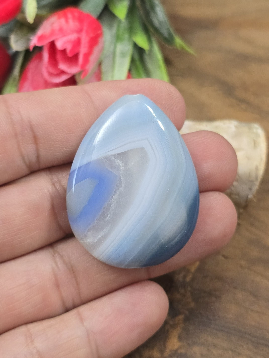 Blauer Achat-Pendant in Tropfenform auf der flachen Hand als Größenvergleich für Kettenanhänger.