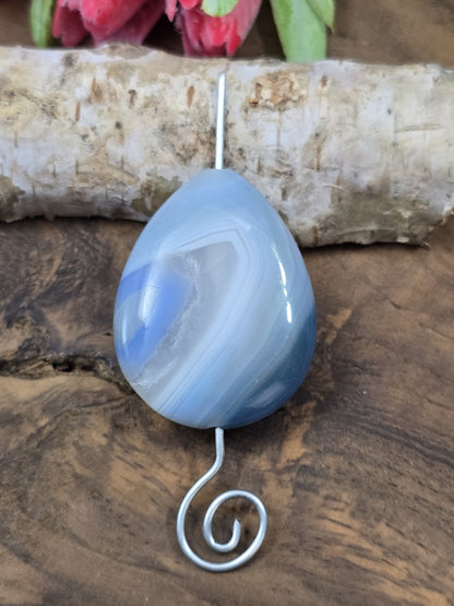 Gefädelter blauer Tropfen-Achat auf einem geschwungenen Metallstift zur Veranschaulichung der Längsbohrung.