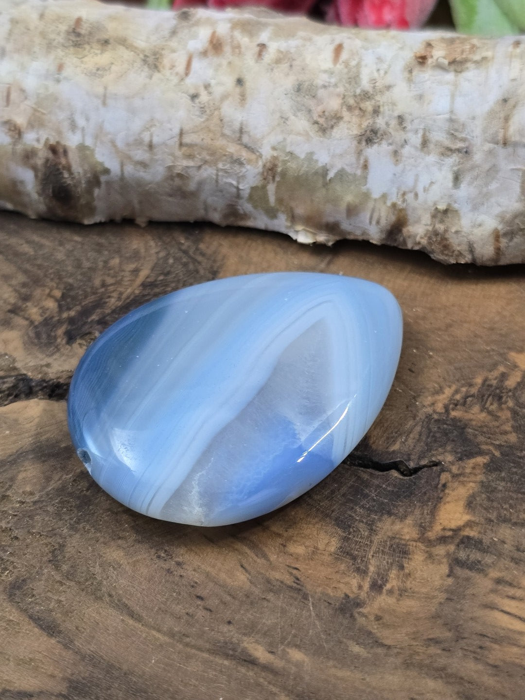 Seitenansicht der flach-gewölbten Form des gebänderten blauen Achat-Edelsteins vor Birkenrinde.