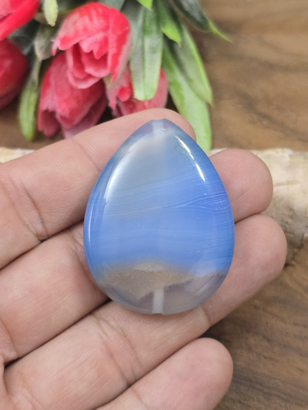 Gebänderter blauer Achat-Pendant in Tropfenform auf der flachen Hand als Größenvergleich für Kettenanhänger.