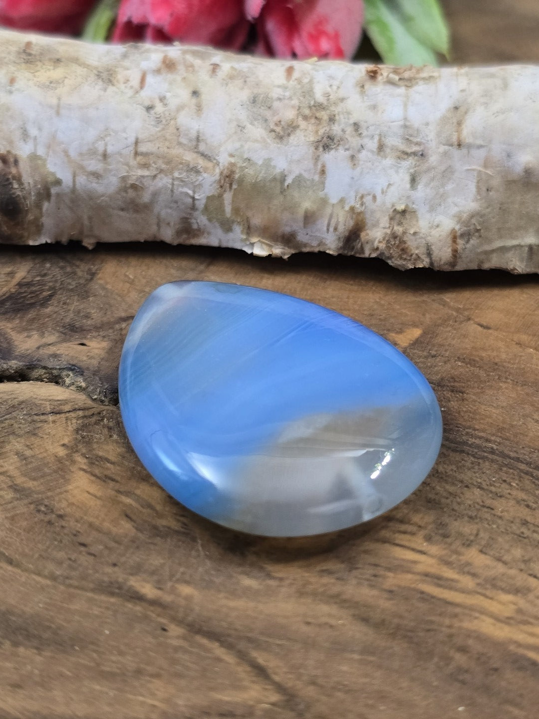 Perspektivische Ansicht des flachen blauen Achat-Anhängers auf Holz mit Sicht auf die untere Bohröffnung.