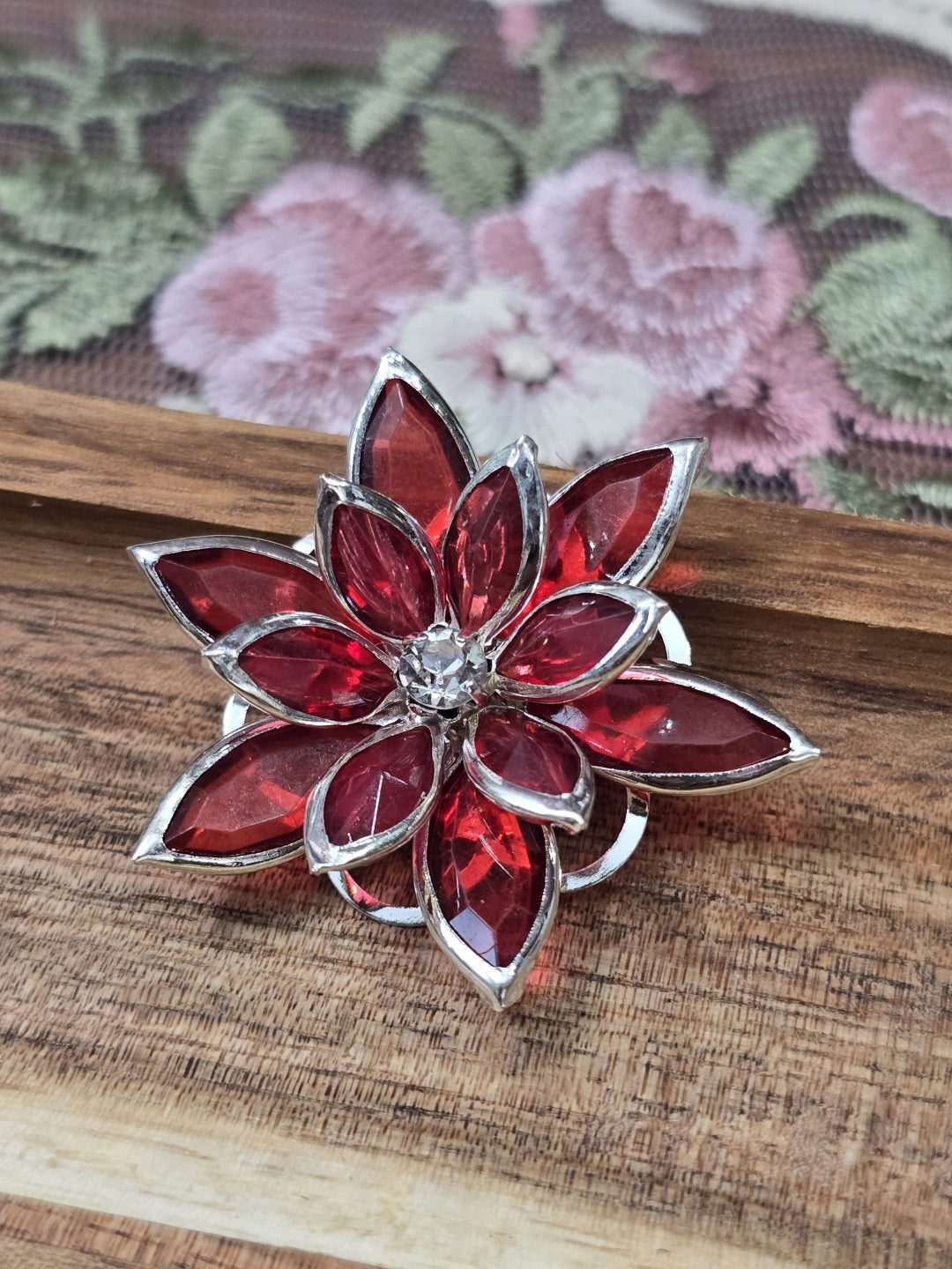 Roter Blüten-Cabochon 31mm mit silberner Fassung und Strass-Mitte auf Holzgrund.