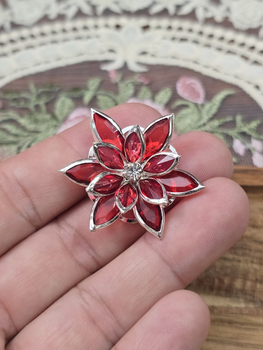 Blütenförmiger Schmuck-Cabochon in Rot und Silber auf Hand gehalten als Größenvergleich.
