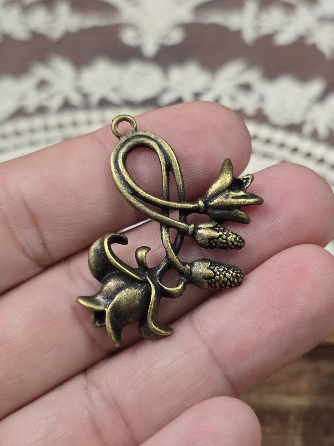 Blumen-Schmuckanhänger 34x29mm in Bronze-Optik auf den Fingern gehalten als Größenvergleich.