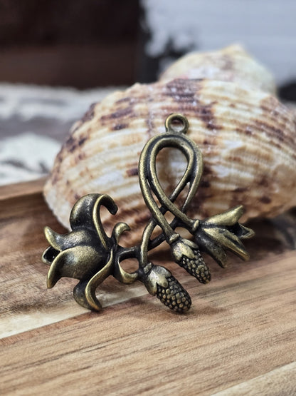 Filigraner Blumen-Anhänger in Antikbronze dekoriert vor einer Muschel auf Holz.