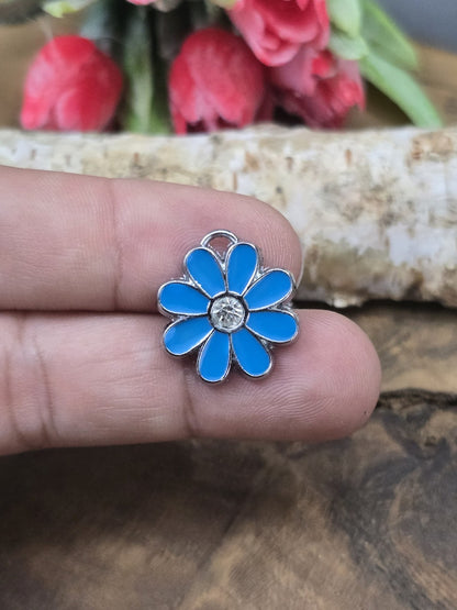 Ein blauer Emaille-Blumenanhänger (18 mm) auf einer Fingerspitze zum praktischen Größenvergleich für die eigene Schmuckherstellung.