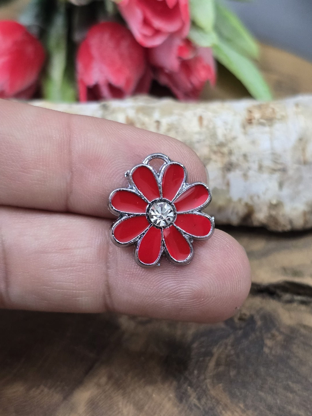 Ein roter Emaille-Blumenanhänger (18 mm) auf einer Fingerkuppe präsentiert als Größenbeispiel für DIY-Schmuck und Bastelarbeiten.