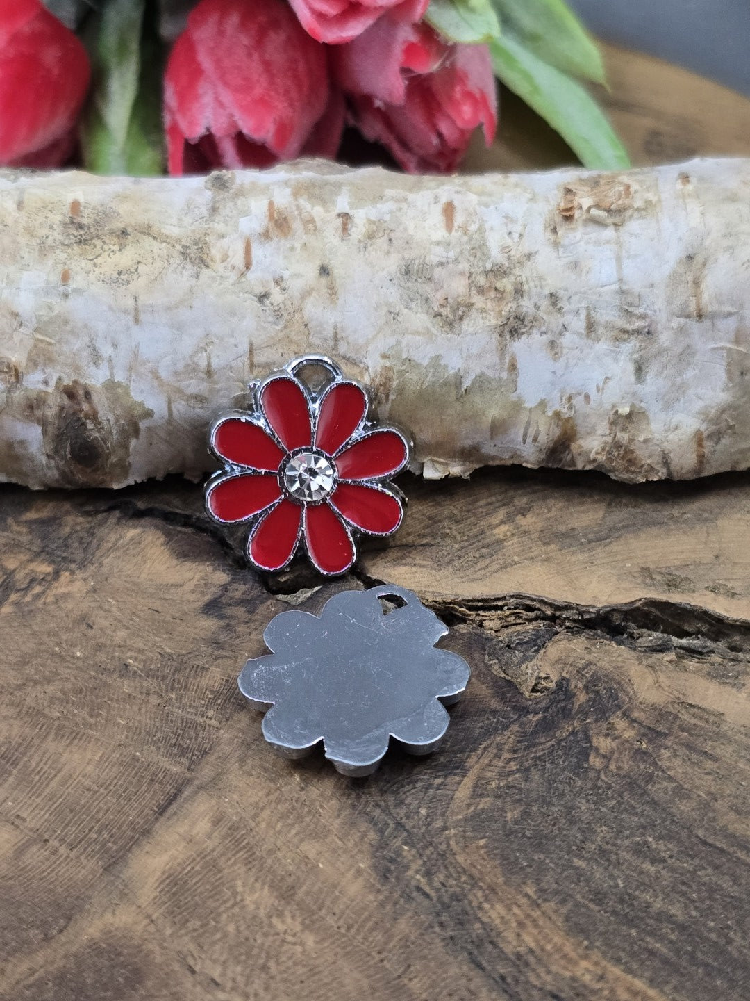 Ein roter Edelstahl-Blumenanhänger von vorne und ein zweiter von der flachen Rückseite auf Holz liegend zur Ansicht aller Details.