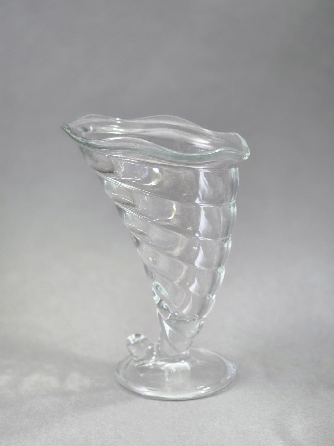 Der Eisbecher steht leicht schräg auf seinem Fuß, die klare Schale zeigt eine gedrehte Struktur und einen geschwungenen oberen Rand.