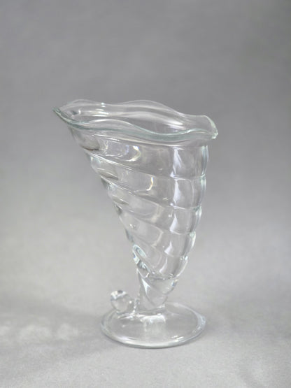 Der Eisbecher steht leicht schräg auf seinem Fuß, die klare Schale zeigt eine gedrehte Struktur und einen geschwungenen oberen Rand.