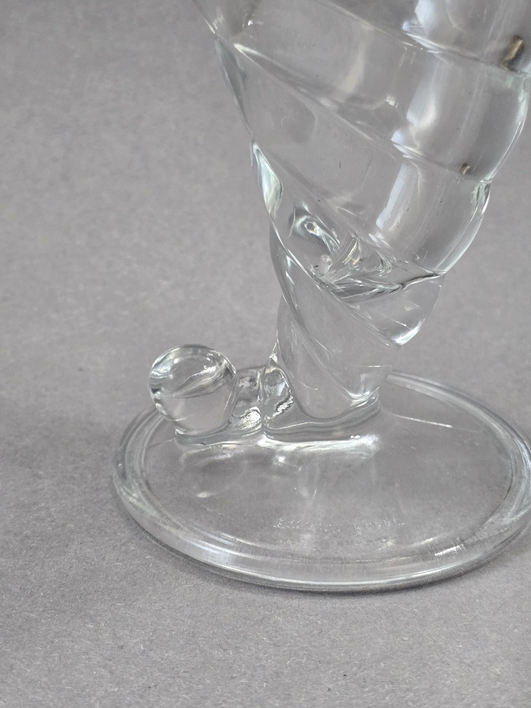 Nahaufnahme vom unteren Bereich des Eisbechers mit rundem Standfuß, kurzem Stiel, spiralförmigem Glasdekor und kleinem Glasknopf am Fuß.