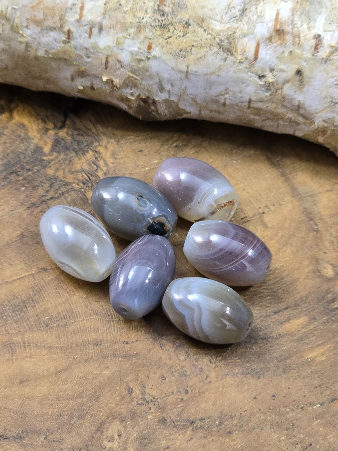 Sechs grau-violette Botswana-Achat-Perlen mit cremefarbener Maserung auf rustikalem Holz arrangiert