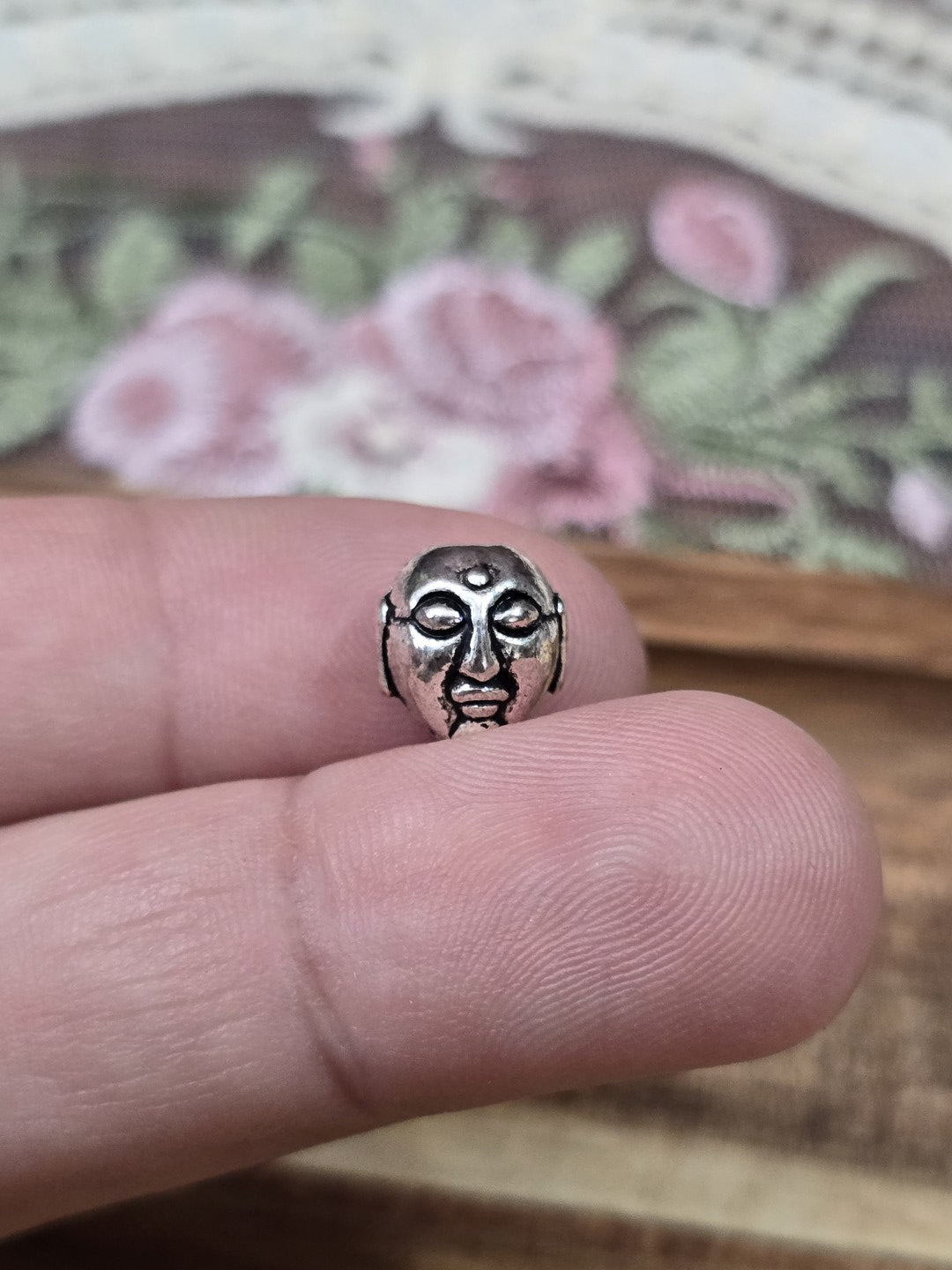 Buddha-Kopf Schmuckperle 9mm in Silber-Optik auf der Fingerkuppe als Größenvergleich.