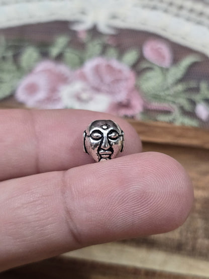 Buddha-Kopf Schmuckperle 9mm in Silber-Optik auf der Fingerkuppe als Größenvergleich.