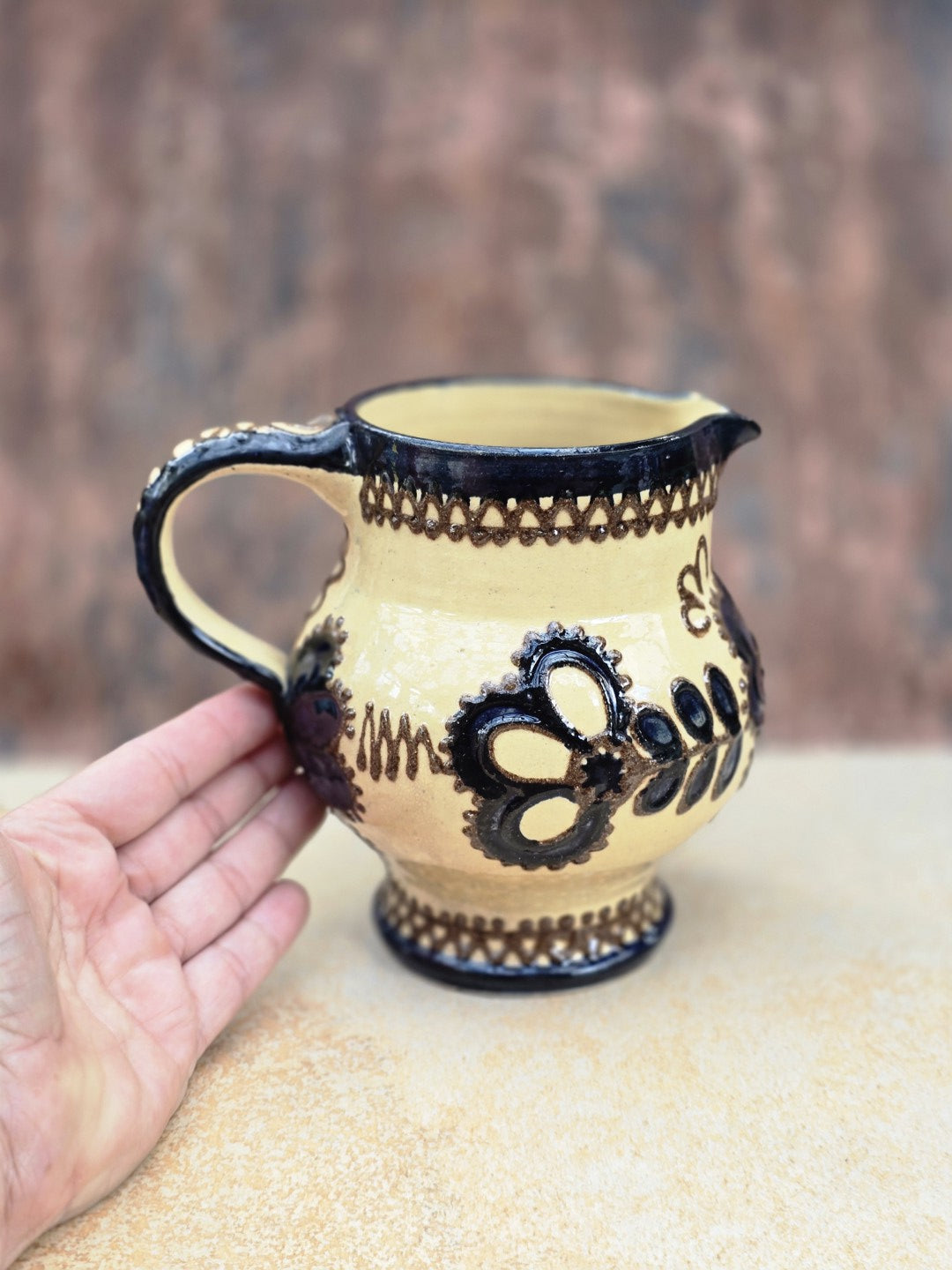 Kleine handdekorierte Kanne aus Vintage-Keramik mit cremefarbener Glasur, dunklem Blumenmuster, bauchiger Form und kleinem Ausguss.