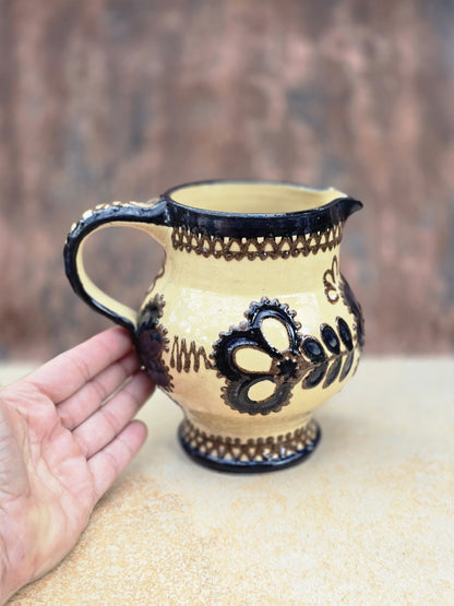 Kleine handdekorierte Kanne aus Vintage-Keramik mit cremefarbener Glasur, dunklem Blumenmuster, bauchiger Form und kleinem Ausguss.
