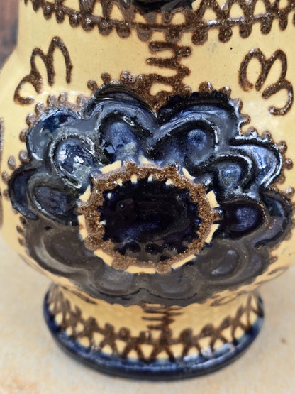 Handwerklich geprägte Keramikkanne im Vintage-Stil mit cremefarbener Glasur, grafischem Blumendekor, bauchiger Form und geschwungenem Henkel.