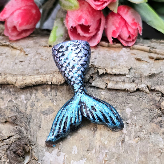 Das Bild zeigt eine handgefertigte Schwanzflosse einer Meerjungfrau aus Kunstharz. Die Flosse ist detailliert bemalt in sanften Farben und hat eine flache Rückseite. Sie eignet sich ideal als Cabochon für Schmuck oder als Dekoration für Bastelprojekte.