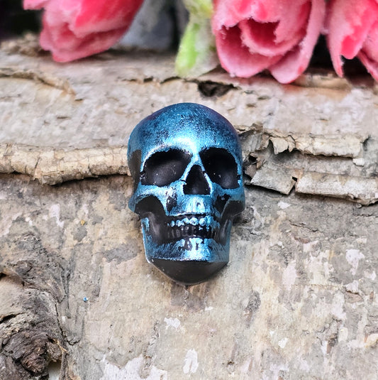 Das Bild zeigt einen Totenkopf-Cabochon in Schwarz mit türkisfarbener Wachsverzierung