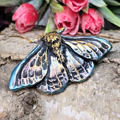 Auf dem Bild ist ein handgefertigter Cabochon in Form einer Deathmoth-Motte zu sehen. Das detailreiche Kunstharzstück zeigt die ausgebreiteten Flügel der mystischen Motte, verziert mit feinen Mustern und Schattierungen. Die Farbgebung betont die Struktur, wodurch das Motiv lebendig wirkt. Die Rückseite ist flach, sodass es sich gut für Schmuck oder Bastelarbeiten eignet. Die Motte liegt auf einem dunklen Untergrund, was ihren geheimnisvollen Charakter unterstreicht.