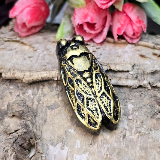 Das Bild zeigt einen handgefertigten Zikaden-Cabochon aus Kunstharz in einer edlen Bronze-Optik. Die Zikade hat eine flache Rückseite mit einem kleinen Loch zwischen den Augen, ideal für die Anbringung einer Anhängeröse.