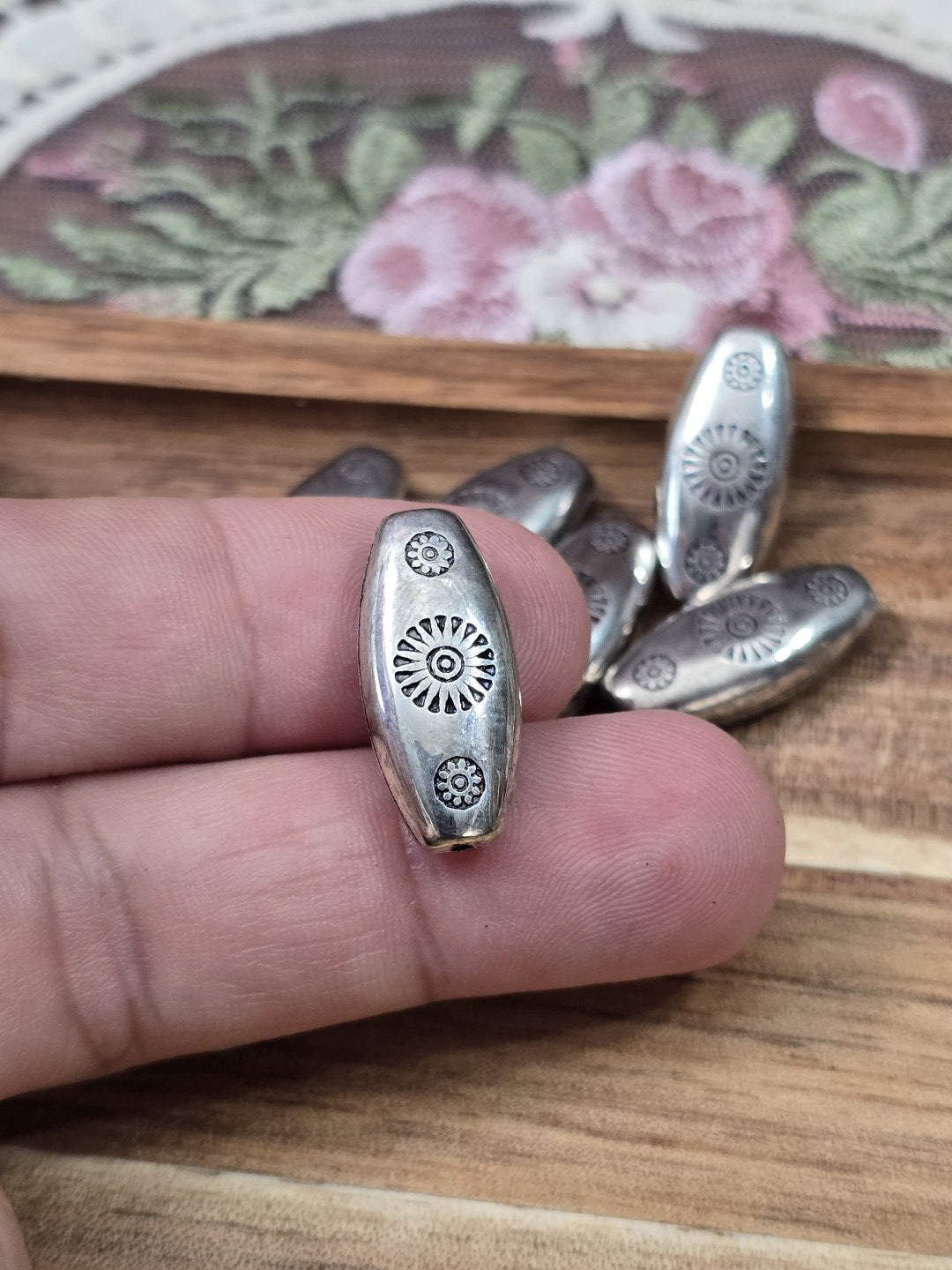 Silberfarbene Navette-Perle 21x10mm mit Vintage-Muster an der Hand gehalten als Größenvergleich.