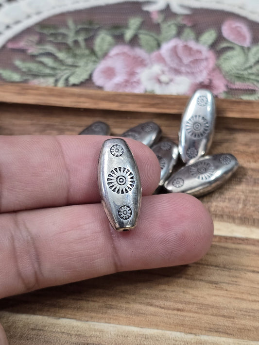 Silberfarbene Navette-Perle 21x10mm mit Vintage-Muster an der Hand gehalten als Größenvergleich.