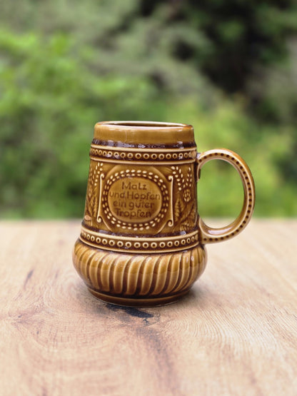 Vorderansicht eines braunen Bierkrugs mit Spruchfeld, Punktbordüre und geripptem Unterteil