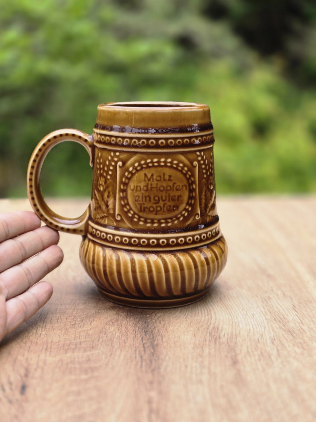 Größenvergleich eines braunen Keramik Bierkrugs mit Henkel, Spruchdekor und Reliefmuster