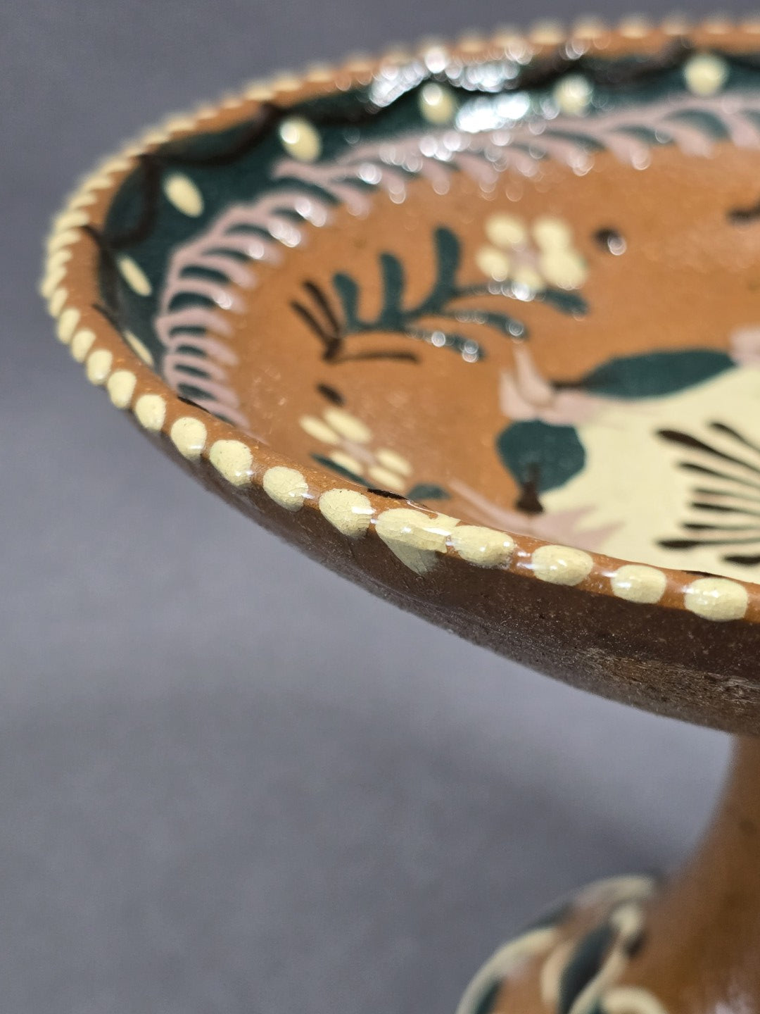 Vintage Keramik-Fußschale mit gepunktetem Rand und grün-braunem Pflanzendekor, Detailaufnahme des glasierten Schalenrands