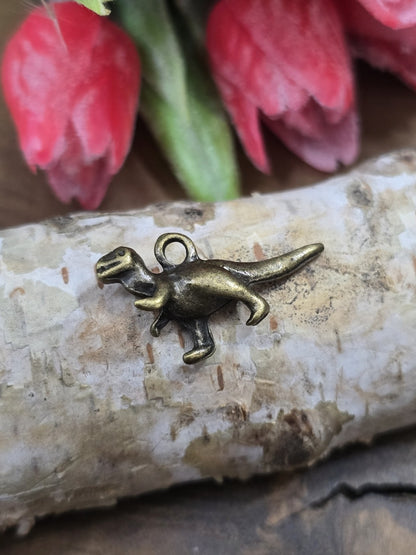 Nahaufnahme eines einzelnen T-Rex Dinosaurier-Metallanhängers (27 mm) mit integrierter Öse auf hellem Birkenholz.