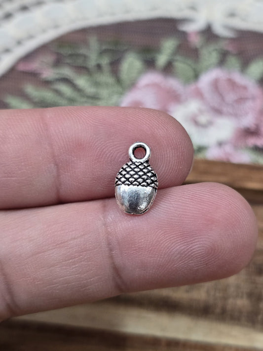 Mini Eichel-Charm 12x7mm in Silber-Optik auf zwei Fingern gehalten als Größenvergleich.