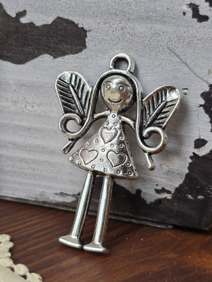 Detailaufnahme des Engels- bzw. Elfen-Charm in Silber-Optik vor dekorativem Vintage-Hintergrund.