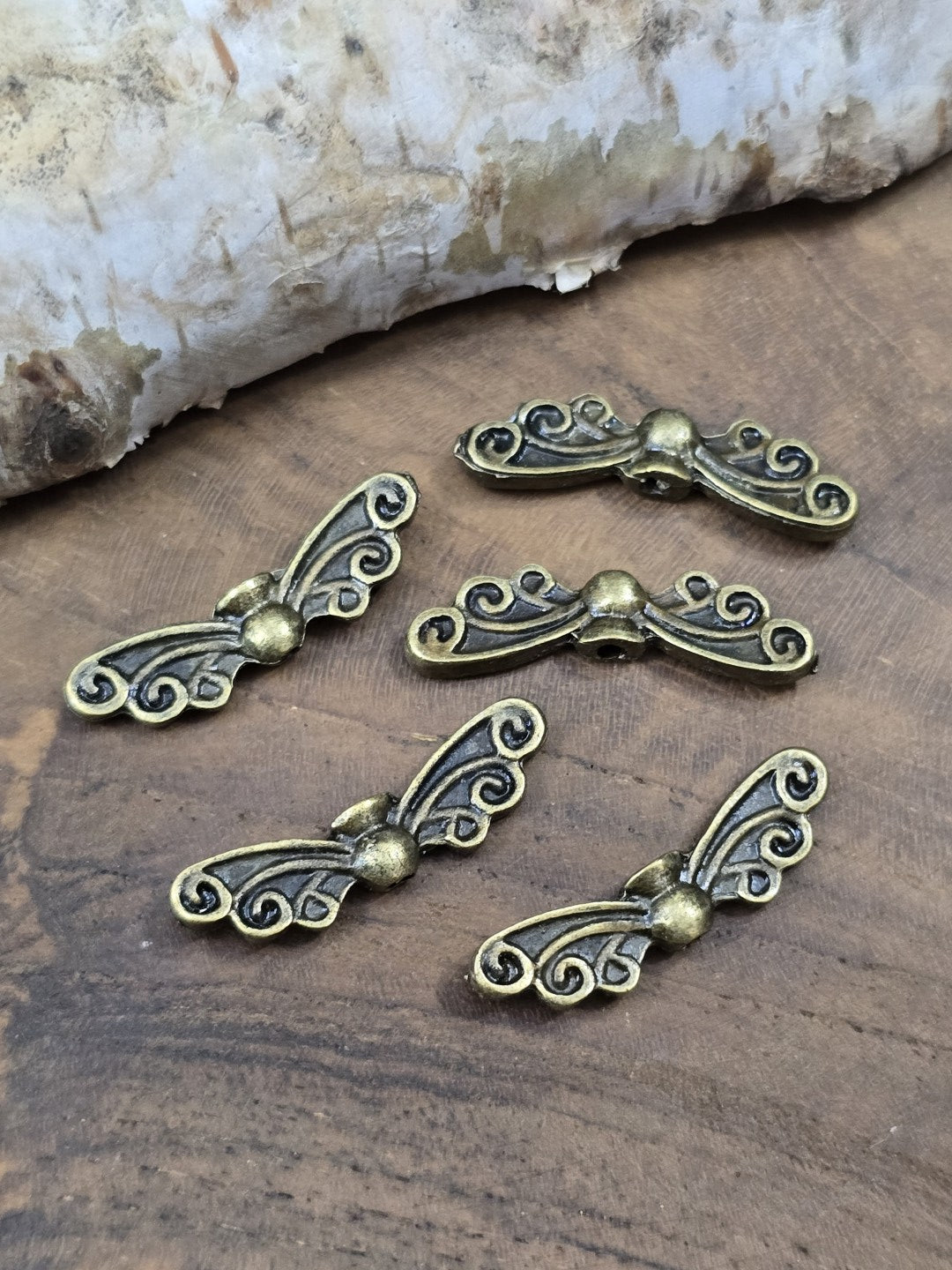Fünf filigrane Engelsflügel-Perlen in Antik-Bronze (22 mm) dekorativ auf Holzgrund arrangiert