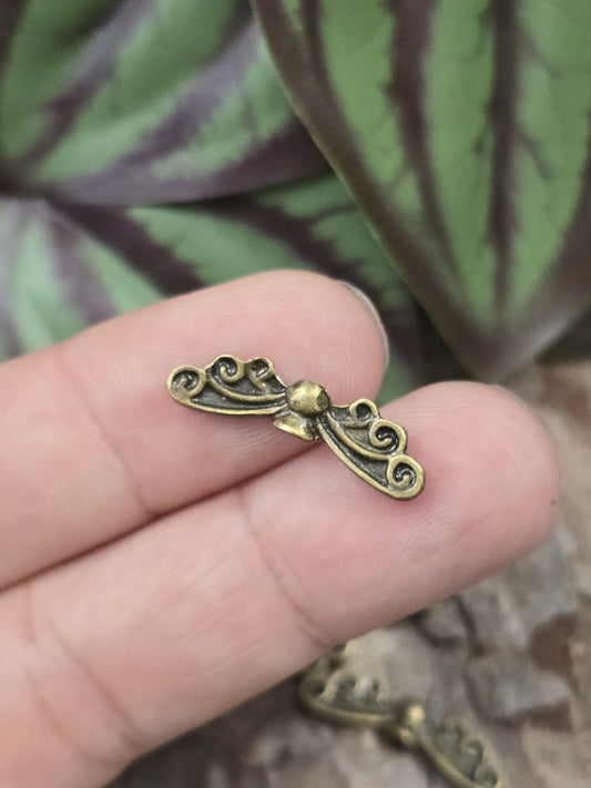 Eine kleine Engelsflügel-Zwischenperle in Antik-Bronze auf einer Fingerkuppe präsentiert als Größenvergleich