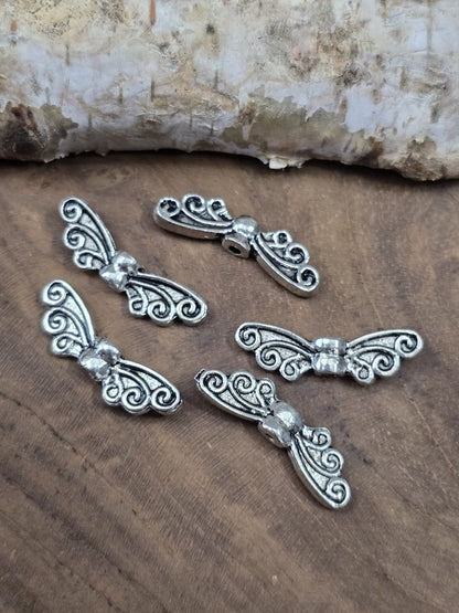 Fünf silberne Engelsflügel-Zwischenperlen (22 mm) schräg arrangiert auf einer rustikalen Holzplatte.