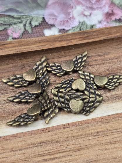 Acht Engelsflügel-Perlen mit Herzmitte in Antikbronze flach liegend auf Holzgrund.