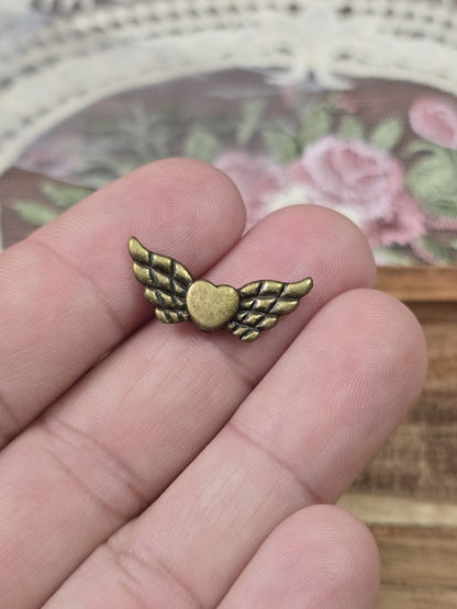 Flügelperle mit Herz 22mm in Bronze-Optik auf zwei Fingern gehalten als Größenvergleich.